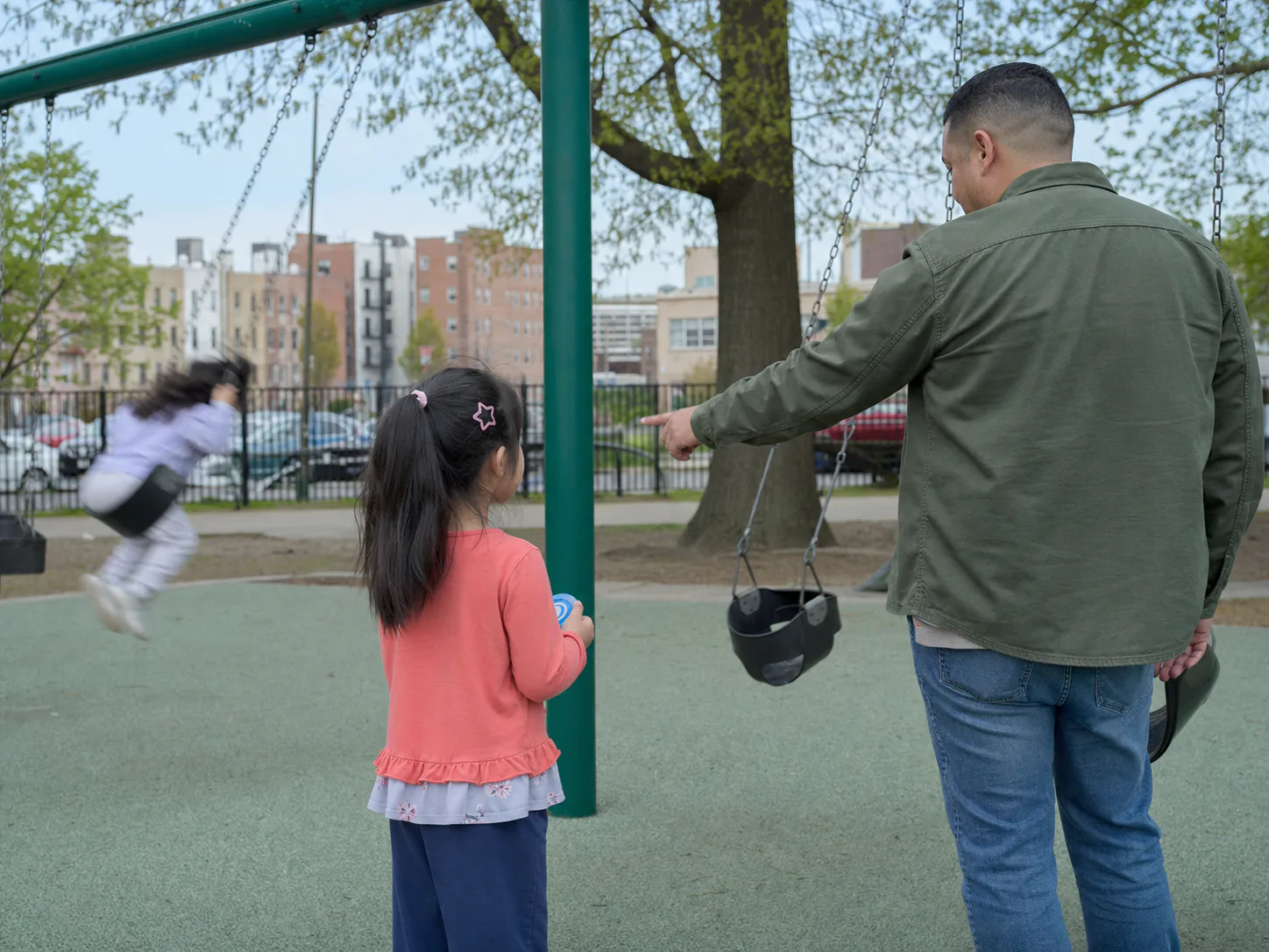 Child waiting for her turn on a playground swing with support nearby